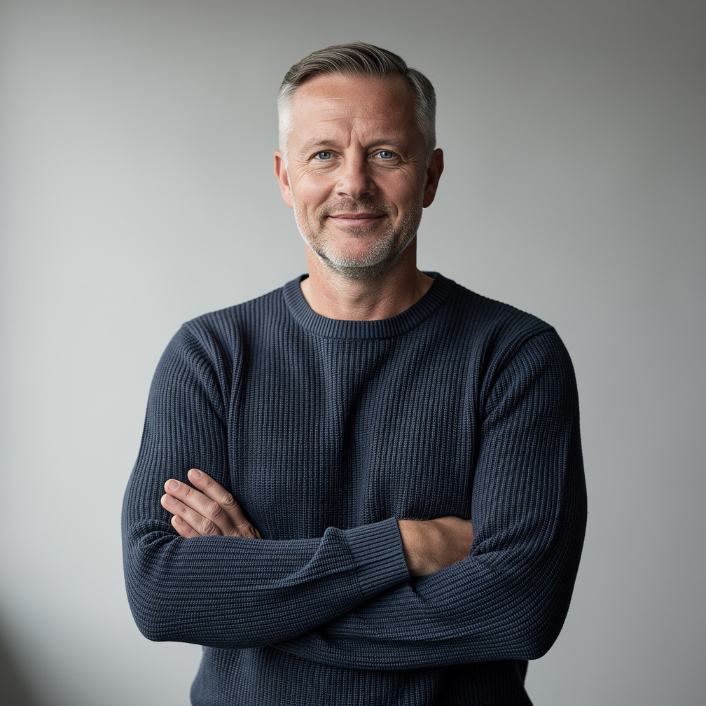 Studio portrait of a Danish male photographer in his forties with short grey hair and a knit sweater